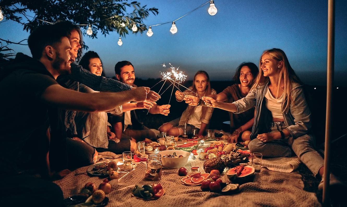Image of a group of friends having an evening picnic and holding sprinklers 