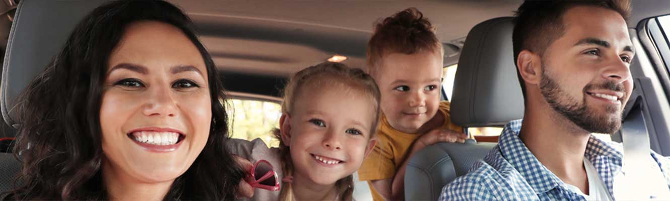 Happy Family of four (Mom, dad, two little girls) in a car headed on a drive. 