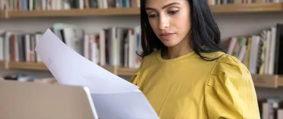 Woman looking down at her computer with a wall of books behind her