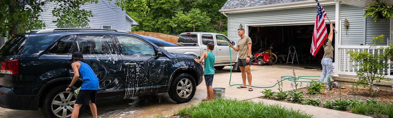 A family of four (Dad, Mom, and two sons) in their driveway washing a car. 