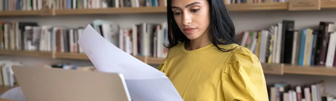 Woman looking down at her computer with a wall of books behinde her